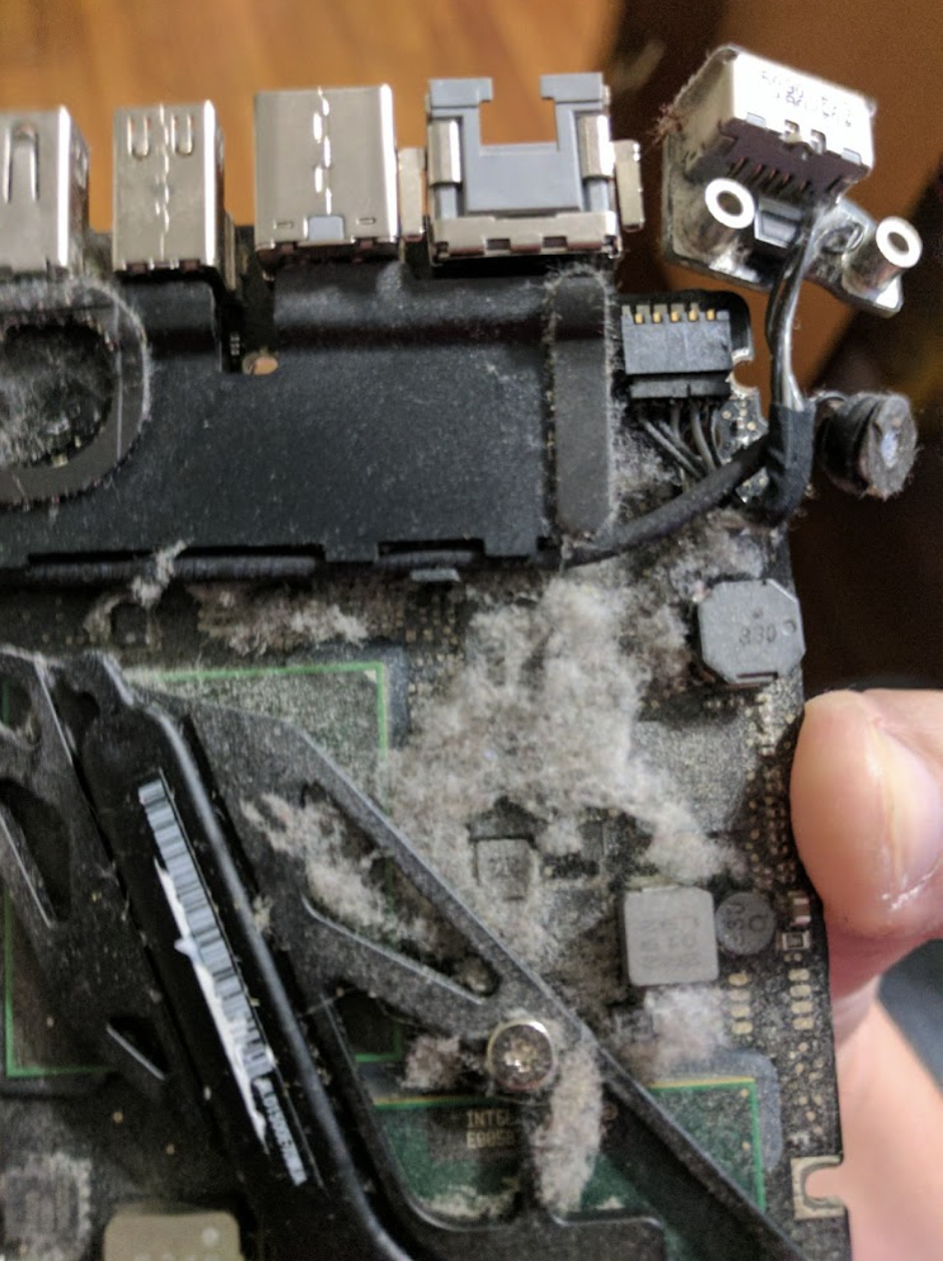 Close-up of a damaged and dust-covered motherboard, with visible debris on ports and components, indicating possible hardware failure.